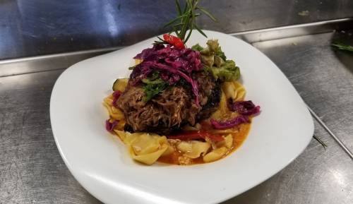 A plated dish featuring pulled meat, colorful vegetables, and pasta, garnished with herbs on a white plate.