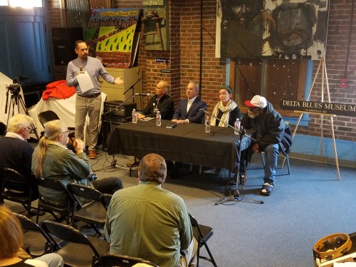 A panel discussion at the Delta Blues Museum, featuring four speakers and an audience in a brick-walled setting.