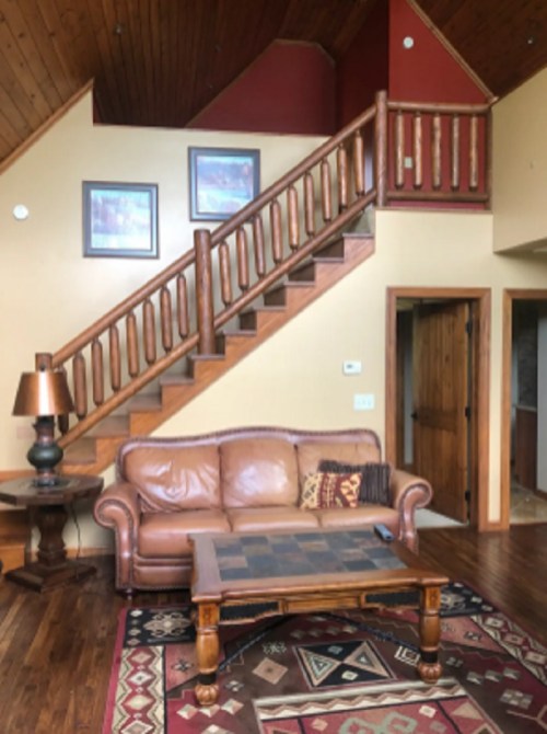 Cozy living room with a leather sofa, wooden coffee table, and a staircase leading to an upper level. Warm, inviting decor.