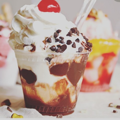 A delicious sundae with whipped cream, chocolate syrup, chocolate chips, and a cherry on top, served in a clear cup.