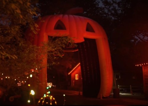 An inflatable pumpkin archway illuminated at night, surrounded by festive lights and decorations.