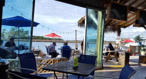 View of a waterfront dining area with tables, umbrellas, and patrons enjoying the scenery on a sunny day.