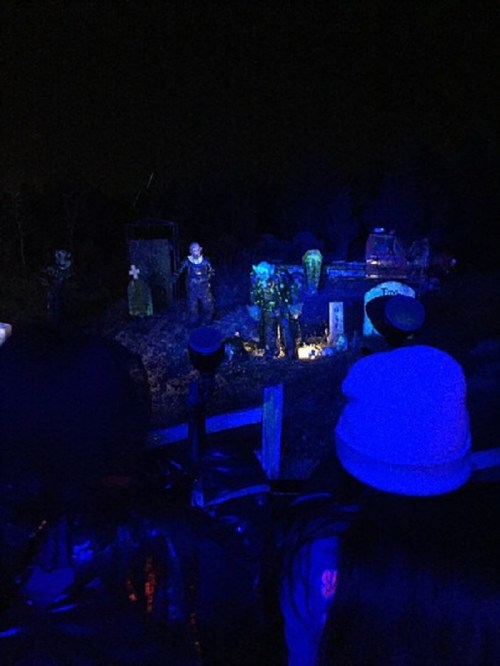 A dark scene with figures in military attire under blue lighting, surrounded by eerie props in a nighttime setting.