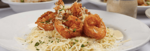 A plate of pasta topped with crispy shrimp and grated cheese, garnished with parsley.
