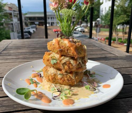 A stacked dish of crispy fried cakes drizzled with sauce, garnished with microgreens, on a wooden table.