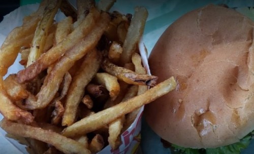 A serving of golden, crispy French fries next to a plain hamburger bun with lettuce.