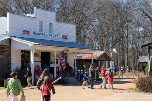 A bustling general store with people walking outside, surrounded by trees and a clear blue sky.