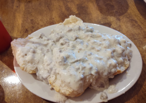 A plate of biscuits topped with creamy sausage gravy, served on a wooden table.
