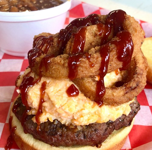 A hearty burger topped with creamy cheese, onion rings, and barbecue sauce, served with a side of baked beans.