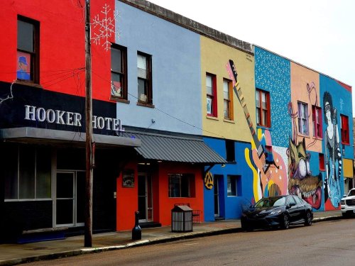 Colorful mural-covered building with the sign "Hooker Hotel" and a parked car in front.