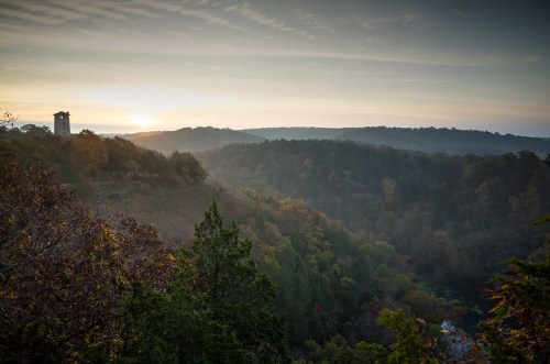 A scenic view of rolling hills at sunrise, with a tower in the distance and autumn foliage in the foreground.