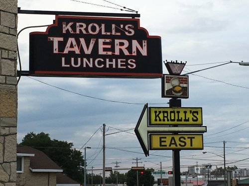Sign for Kroll's Tavern and Kroll's East, featuring the name and lunch offerings against a cloudy sky.