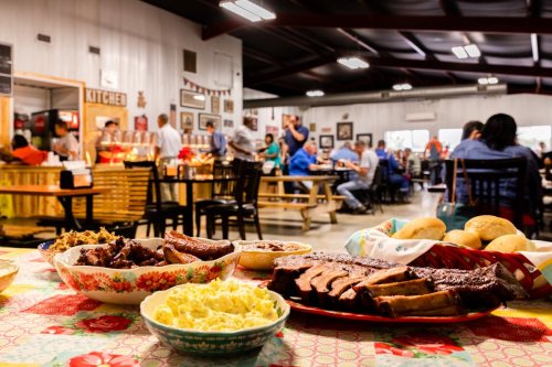 A vibrant restaurant scene with a table of barbecue dishes, including ribs and sides, and diners enjoying their meals.
