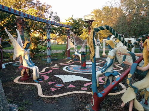 Colorful sculptures of angels and figures in a whimsical garden setting with trees and a circular design on the ground.