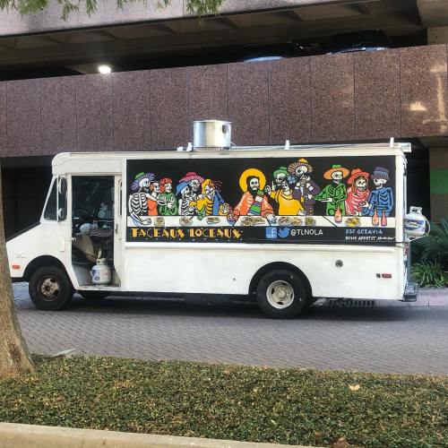 A colorful food truck featuring skeleton characters in festive attire, parked near a building.