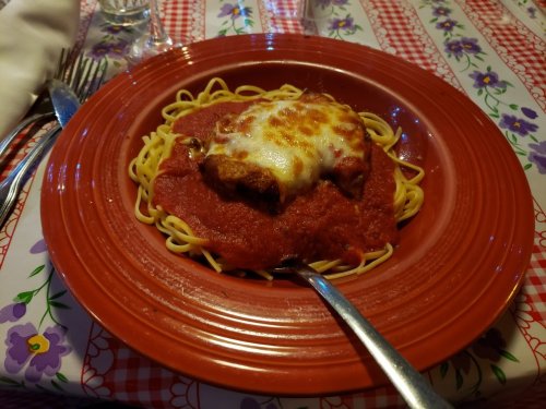 A plate of spaghetti topped with marinara sauce and melted cheese, served on a red patterned tablecloth.