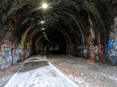 A dimly lit tunnel with a curved path, featuring brick walls and colorful graffiti.