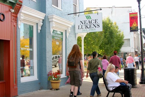 A busy street scene with people walking past shops, including an insurance agency and a sign for Neace Lukens.