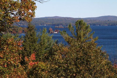 A scenic view of a lake surrounded by colorful autumn trees and distant hills under a clear blue sky.