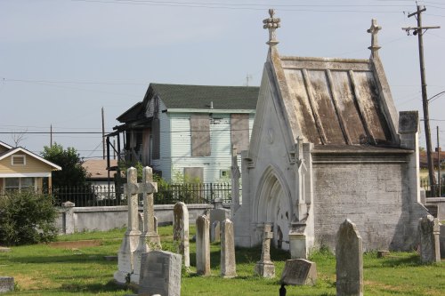 A cemetery with gravestones and a mausoleum, set against a backdrop of an abandoned house.