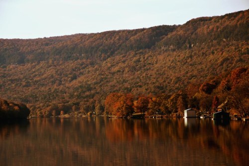 A serene lake surrounded by autumn foliage, reflecting colorful trees and hills in calm waters.
