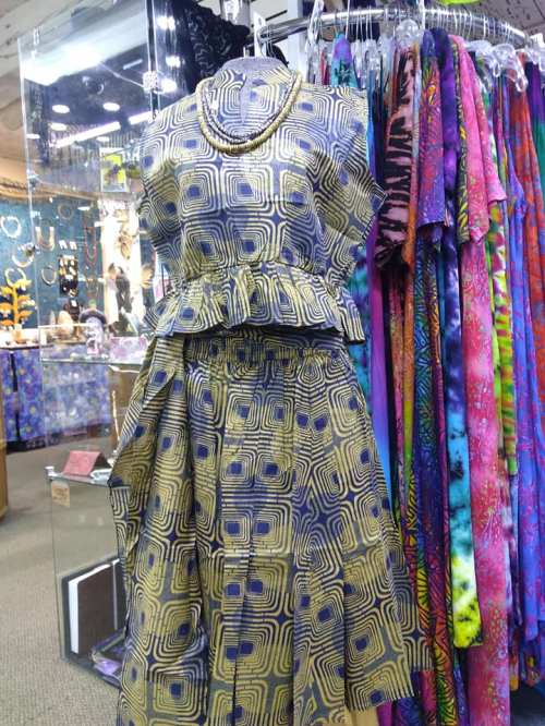 A stylish peplum top and skirt set with a geometric pattern, displayed in a colorful boutique.