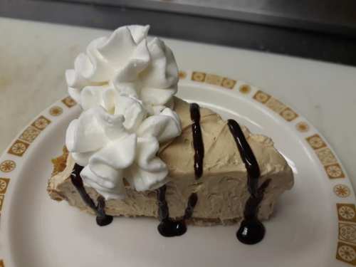A slice of creamy dessert topped with whipped cream and chocolate drizzle on a decorative plate.