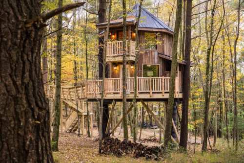 A wooden treehouse with balconies, nestled among trees in a colorful autumn forest.