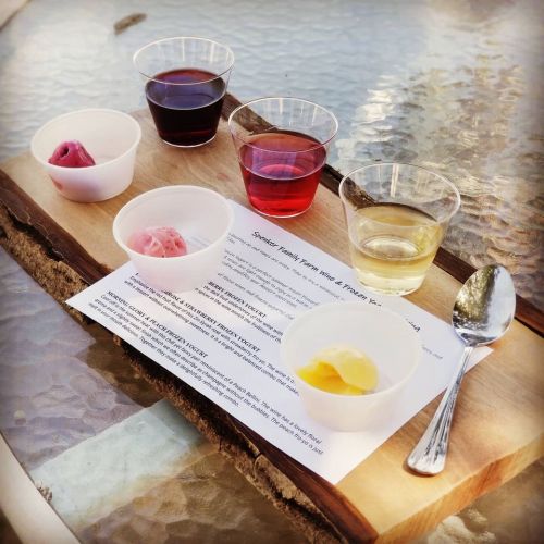 A wooden board with five small cups of colorful drinks and sorbet, accompanied by a menu on a glass table.