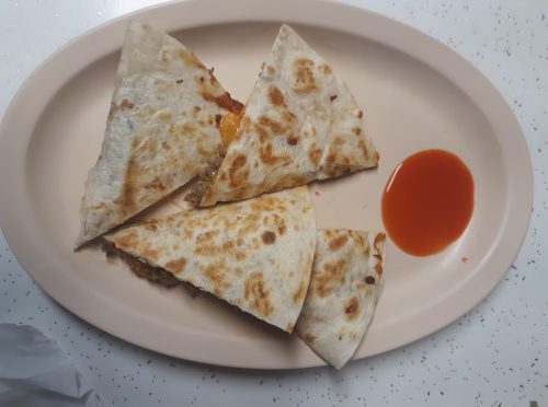 A plate with four triangular quesadilla pieces and a small serving of red sauce on the side.