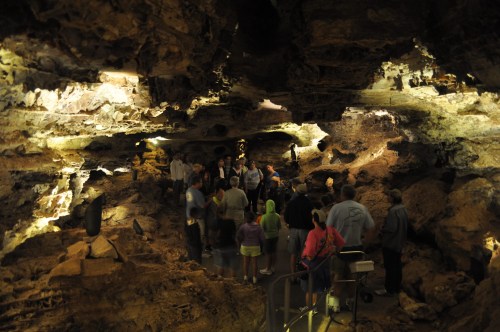 A group of people tours a dimly lit cave, surrounded by rock formations and illuminated by soft lighting.
