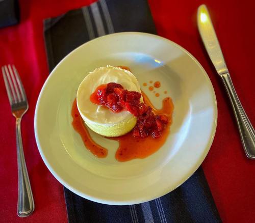 A dessert on a plate featuring a creamy layer topped with strawberry sauce, served on a red tablecloth.
