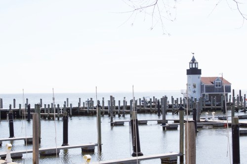 A serene marina with empty docks and a lighthouse in the background, under a clear blue sky.