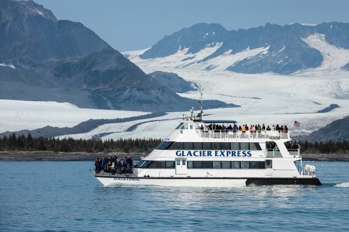 A tour boat named "Glacier Express" sails on calm waters with a glacier and mountains in the background.