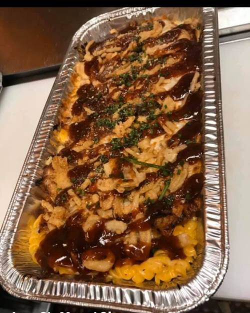 A large tray of macaroni and cheese topped with barbecue sauce, crispy onions, and herbs.