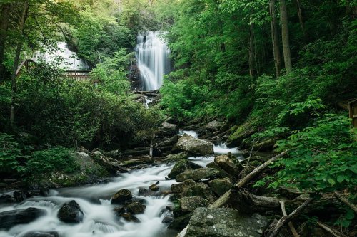A serene waterfall cascades through lush greenery, surrounded by rocks and flowing water in a tranquil forest setting.