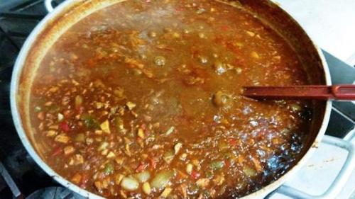 A large pot of simmering stew with vegetables and spices, steam rising from the surface.