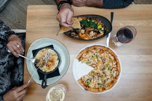 A table with a pizza, a dish in a skillet, and a plate of food, accompanied by glasses of wine.