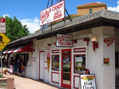 A colorful candy and gift shop with a red and white awning, featuring signs and a busy sidewalk in front.