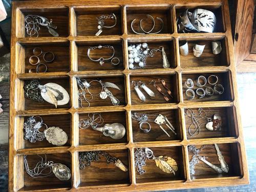 A wooden jewelry organizer filled with various silver and metal pieces, including rings, necklaces, and earrings.