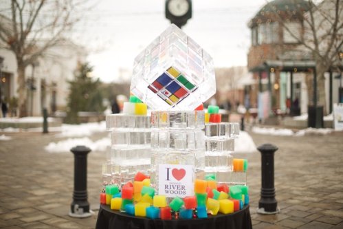 A large ice sculpture with colorful cubes at its base, featuring a sign that says "I ❤️ RIVER WOODS." Snowy outdoor setting.