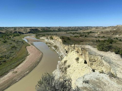 A winding river flows through a rugged landscape of hills and cliffs under a clear blue sky.