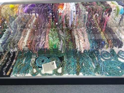 A display case filled with colorful strands of beads and gemstones in various shapes and sizes.