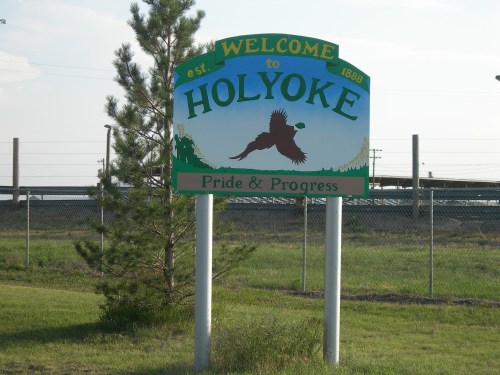 Welcome sign for Holyoke, established 1888, featuring a bird and the text "Pride & Progress" against a green background.