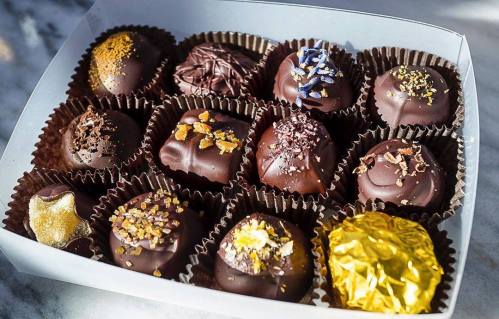 A box of assorted chocolate truffles, each uniquely decorated with toppings like nuts, flowers, and gold foil.