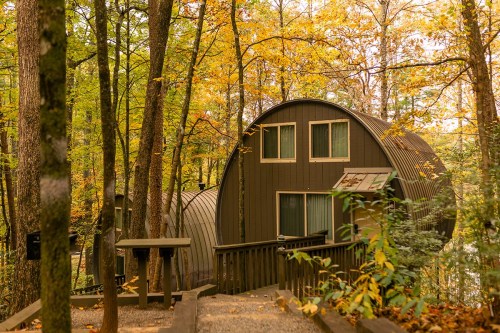 A modern, curved cabin nestled among colorful autumn trees in a serene forest setting.
