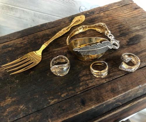 A vintage fork beside a decorative bowl and various silver rings on a rustic wooden surface.
