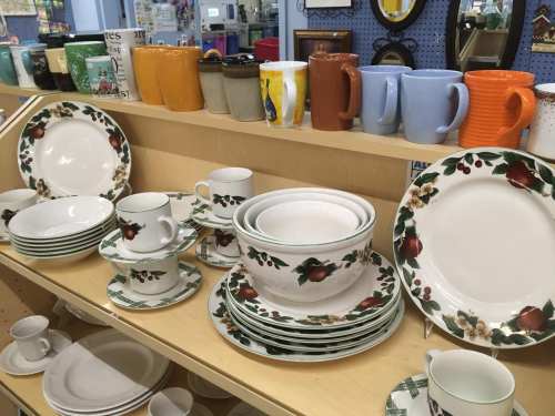 A display of various ceramic dishes and mugs, featuring floral designs and different colors, on a wooden shelf.