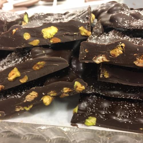 Close-up of dark chocolate bark with pistachios and a sprinkle of salt, stacked on a tray.