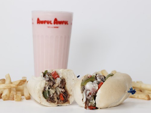 A split sandwich filled with beef and vegetables, served with fries and a pink milkshake in a branded cup.